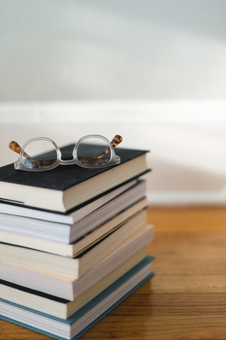 A stack of eight books with reading glasses sitting on top