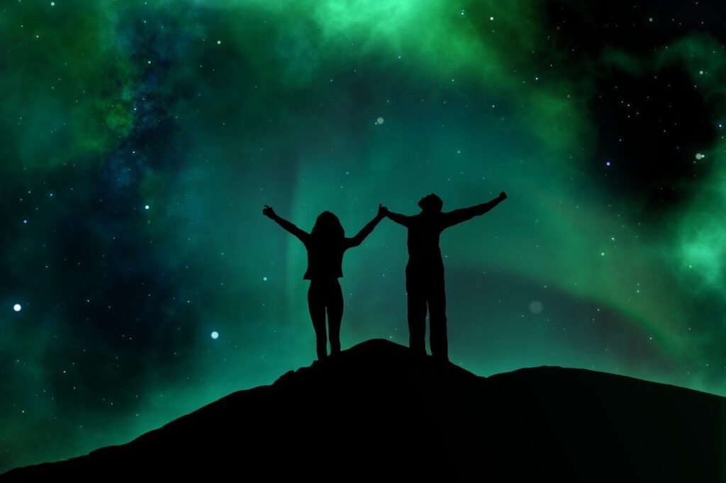 A couple holding hands staring up into the green night sky filled with stars.