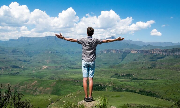 A man stands triumphantly with arms open, overlooking a scenic mountain range and admiring his proven growth strategies