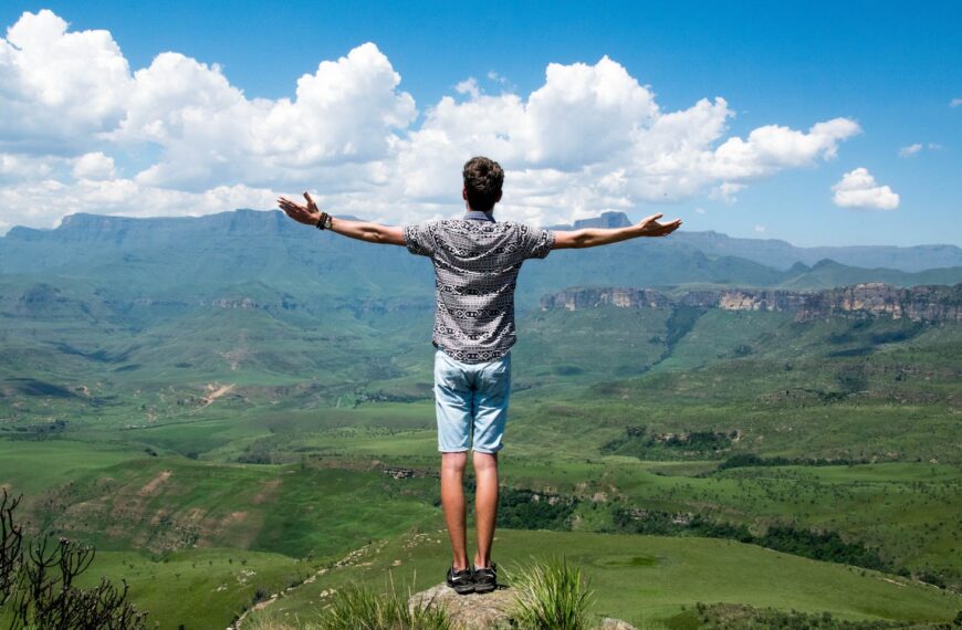 A man stands triumphantly with arms open, overlooking a scenic mountain range and admiring his proven growth strategies