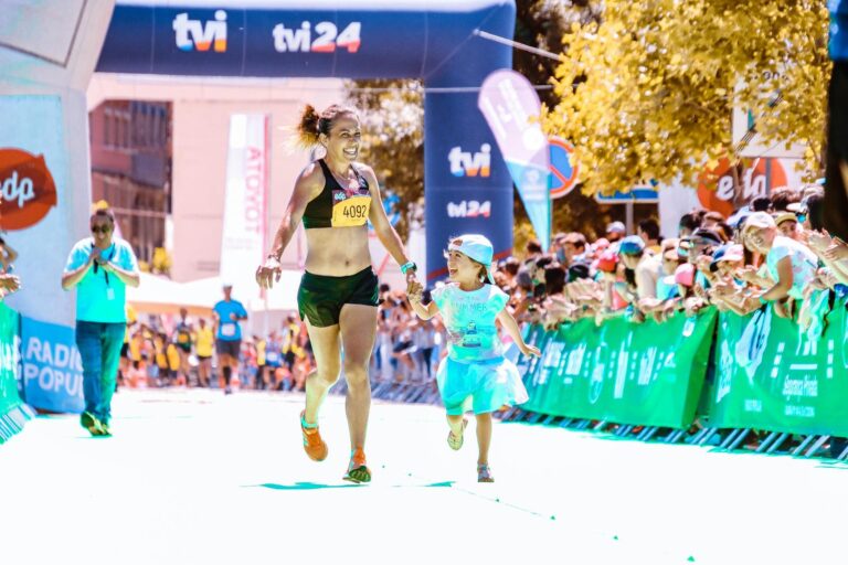 A joyful mother and daughter cross the marathon finish line hand in hand, exuding happiness and energy.