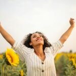 She is a joyful woman with arms raised in a sunflower field, embracing freedom because she has mastered manifestation successfully