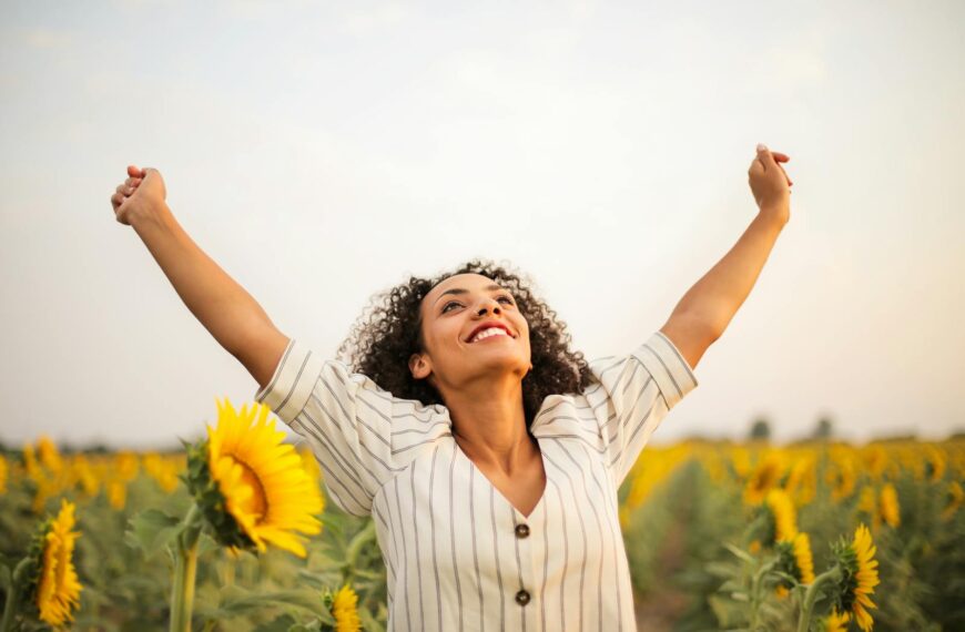 She is a joyful woman with arms raised in a sunflower field, embracing freedom because she has mastered manifestation successfully