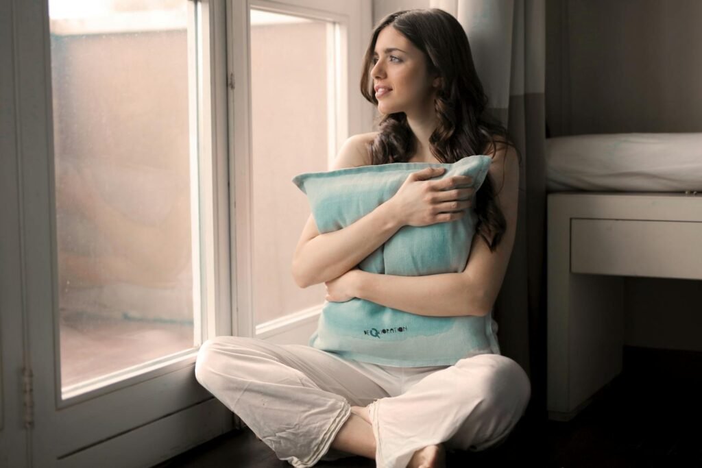 Serene woman sitting indoors, embracing positive thinking, lost in thought by a bright window.