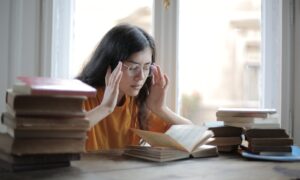 A young woman searching for the law of attraction secrets while reading and studying surrounded by books.