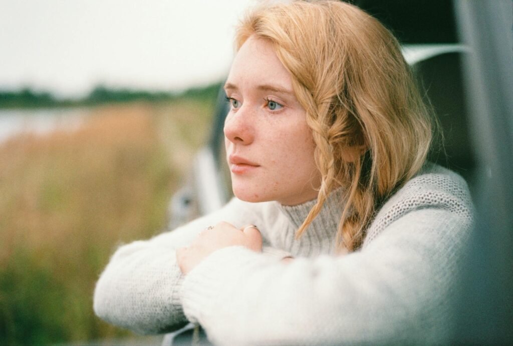 A woman with braided blonde hair gazes thoughtfully from a car window, capturing a serene moment.