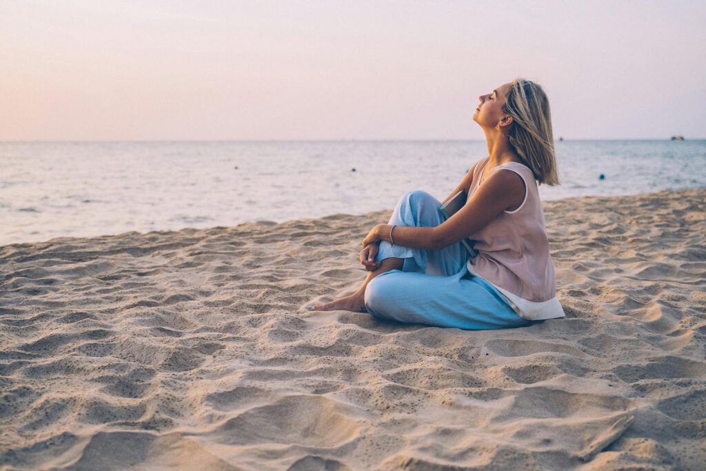 It is peaceful as a woman relaxes on a sandy beach, enjoying the sunset.