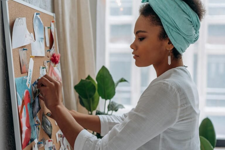 Women create a vision board with images in a stylish home setting, showcasing creativity and focus.