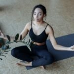 A young woman is sitting cross-legged in peaceful yoga meditation indoors—manifestation techniques concept.