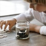 A young child collects coins in a jar labeled 'For Barbie Castle, ' which symbolizes saving and prosperity.