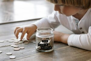 A young child collects coins in a jar labeled 'For Barbie Castle, ' which symbolizes saving and prosperity.