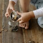 A child adds coins into a glass jar labeled for wealth and prosperity