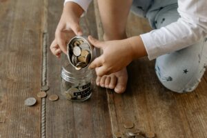 A child adds coins into a glass jar labeled for wealth and prosperity