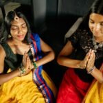 Two women in traditional Indian dresses meditate with praying hands indoors leveraging the law of attraction