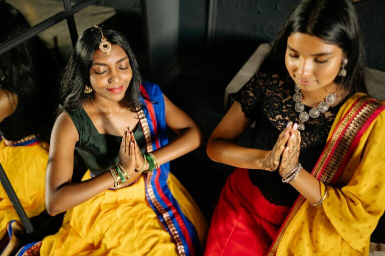 Two women in traditional Indian dresses meditate with praying hands indoors leveraging the law of attraction