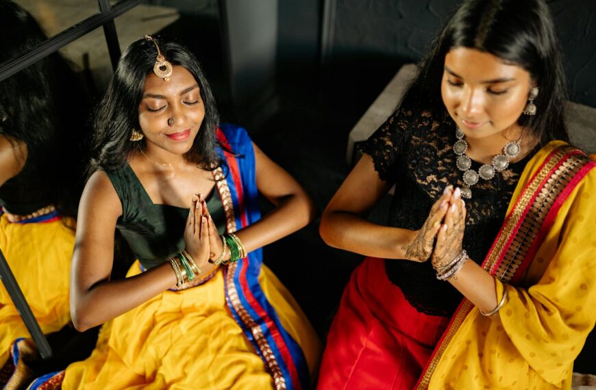 Two women in traditional Indian dresses meditate with praying hands indoors leveraging the law of attraction